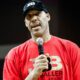 LaVar ball holding a microphone wearing red bbb shirt and black hat