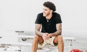 lonzo ball sitting on a bench smiling with a black shirt