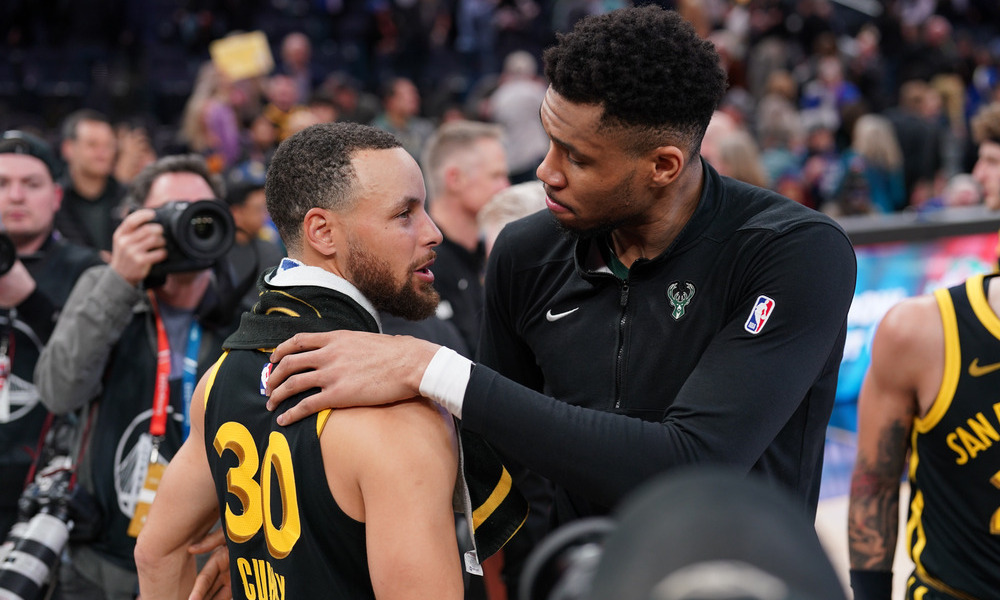 Giannis Antetokounmpo and Steph Curry embracing after a game.
