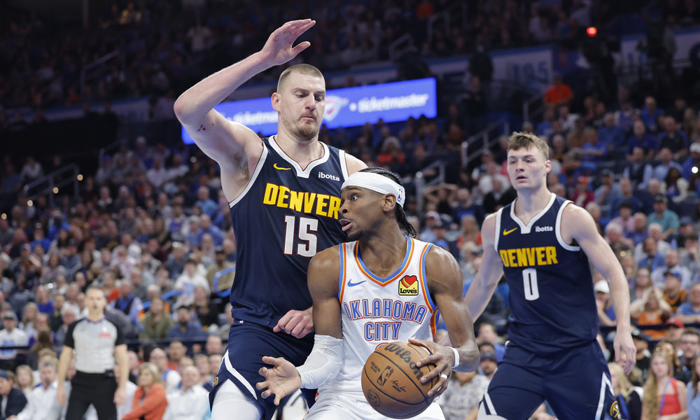 Nikola Jokic defends Shai Gilgeous-Alexander, who is driving to the basket.