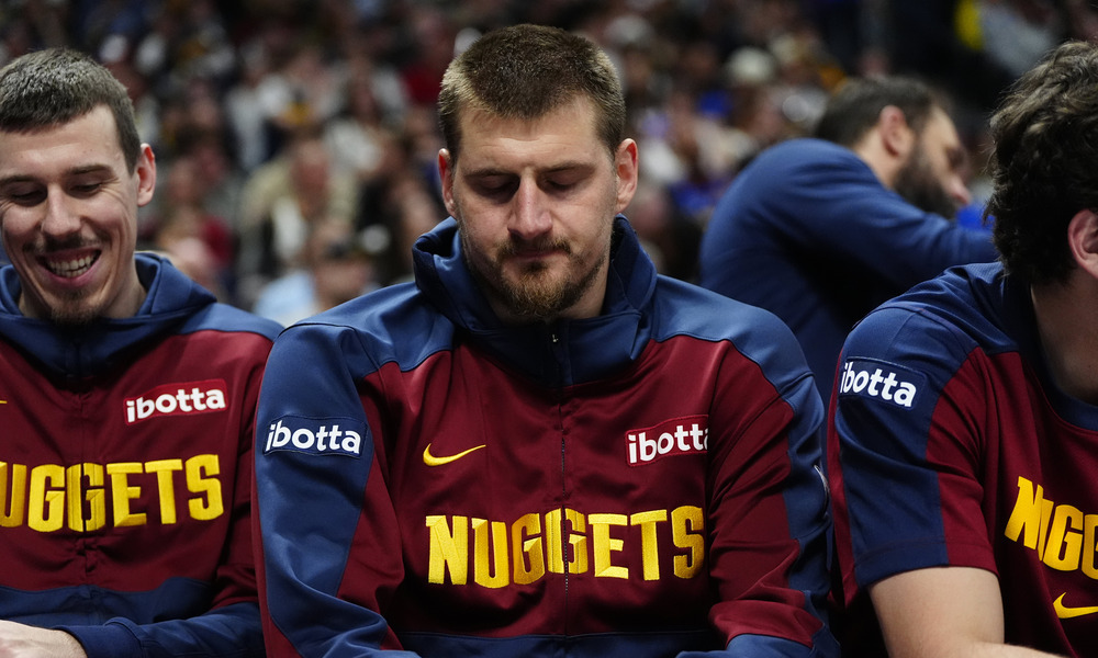 Nikola Jokic sitting on the bench with his teammates.